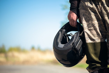 Biker with a helmet in hands is standing on the road close up.