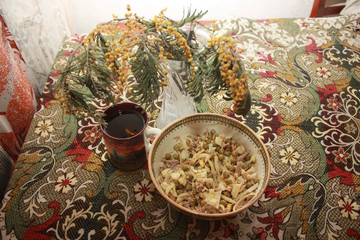 A bowl with olivier salad, a cup of tea and a bouquet of mimosa flowers on a table covered with a colored tablecloth.