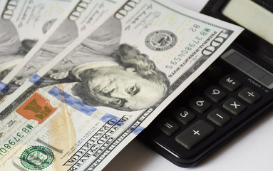 blurred light background, a pile of dollars banknotes on a white background and calculator, business concept