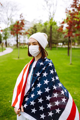 Girl in protective sterile medical mask and with american flag in her hand. The concept of preventing the spread of the epidemic and treating coronavirus, pandemic in quarantine city. Covid -19.