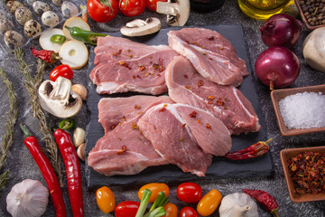 Pork steaks, fresh vegetables, spices close-up on a textured background top view