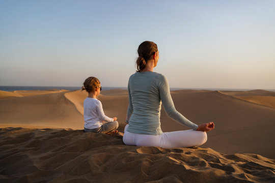 Mother and daughter practicing yoga in sand dunes at sunset, Gran Canaria, Spain