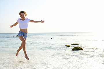 Fototapeta na wymiar Beautiful woman running and jumping for joy on the beach