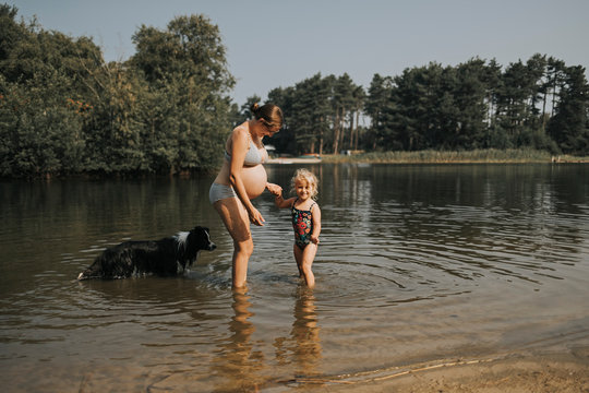 Netherlands, Schiermonnikoog, pregnant mother with daughter and Border Collie in a lake
