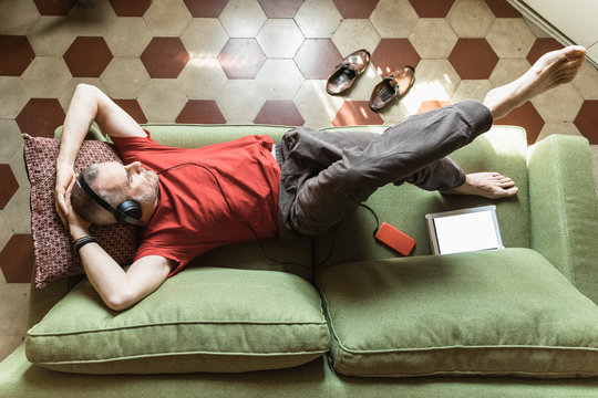 Mature man lying on sofa and using tablet, listening music