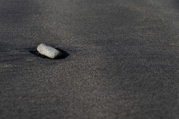 Lonely rock on black sand beach macro photography. Silky black beach texture with shallow depth of field. Minimalistic black background. Tenerife voulcanic sandy shore.