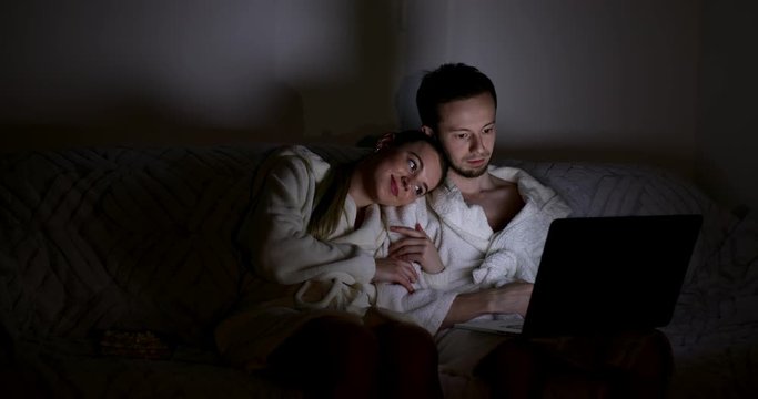 young family man and woman watching movie on laptop at home sitting on couch together. Surfing internet, stream content and seeing video