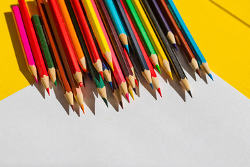 Rough shadow. Bright sunshine. Retro yellow wooden background. In the center, a sheet of paper with drawings and around lined with pencils of different colors.