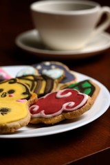 Cookies made with butter and decorated with various figures such as a cat, chicken, bee, mushrooms, placed on a glass plate and a wooden base, diffuse bottom of a cup of coffee.