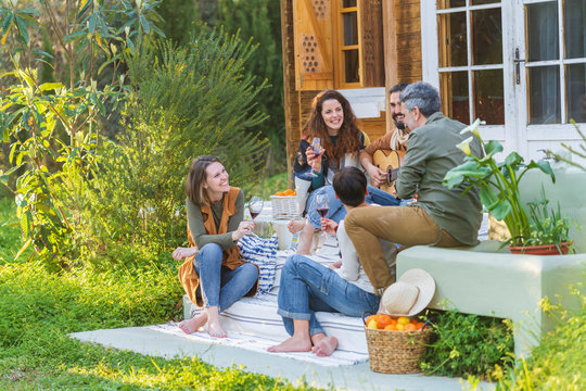 Friends playing music on the guitar and drinking wine outside a cabin in the countryside