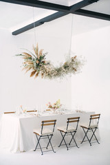 festive table with a floral bouquet, candles, chairs and a flower garland