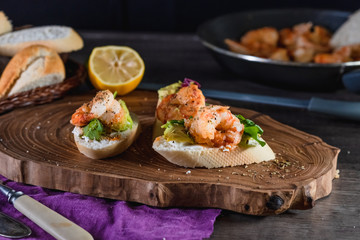 Sandwiches with shrimp, cheese and avocado on a wooden tray on the table, dark background. The concept of nutrition and beautiful serving of food