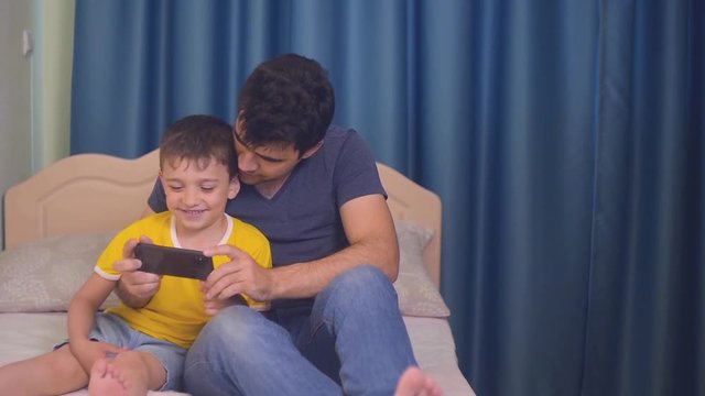the boy and his father look at the smartphone screen, parents and children get acquainted with new technologies, the family uses gadgets to communicate