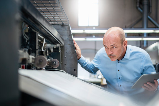 Businessman with tablet examining machine in a factory