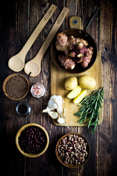 Cutting board, wooden ladles, garlic, rosemary, potatoes, salt and pepper, Jerusalem artichokes and bowls with various beans and lentils