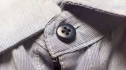 Macro shot of the top black button of a light shirt made of fabric in a strip and collar
