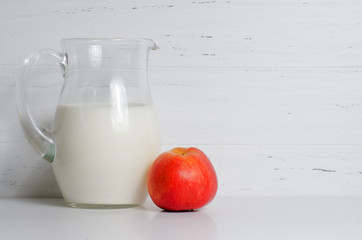 Milk in a glass jug and an apple. The concept of natural and healthy food. White background. Copy...