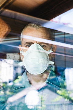 Mature man with protective mask looking through of the window, looking at camera
