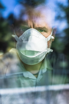 Mature man with protective mask looking through of the window, looking at camera