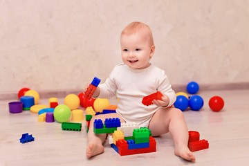 Obraz premium little baby in white clothes sits and plays with a multi-colored designer at home, child development