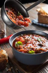 Borsch is poured into a bowl of soup ladle, traditional Ukrainian vegetable soup made from beets, carrots, tomatoes, potatoes, cabbage, herbs and garlic, close-up, shallow depth of field, selective