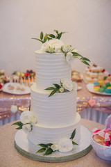 Wedding cake.Three tiers of white, decorated with white flowers.On a table in a restaurant