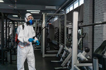 Cleaning and Disinfection in crowded places amid the coronavirus epidemic Gym cleaning and disinfection Infection prevention and control of epidemic. Protective suit and mask and spray bag COVID-19