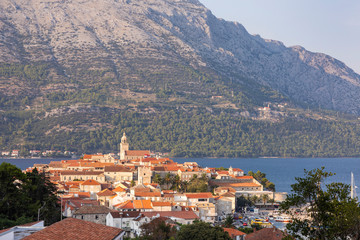Fototapeta na wymiar Korcula island with the cathedral, the city and the port on a sunny day during sunset in summer. Beautiful old venetian architecture, trees and mountains creating an idyllic scenery