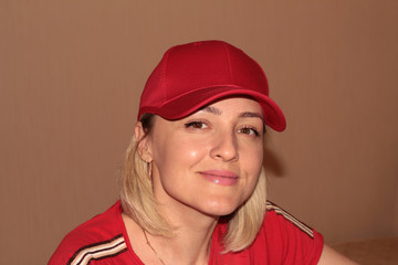 A girl in a red cap and t-shirt smiles on a beige background. A blonde in red clothes.