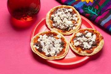 Mexican red sopes with cheese and beans on pink background