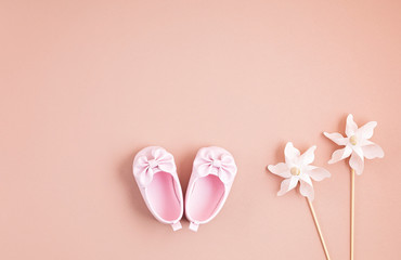 Cute newborn baby girl shoes with festive decoration over pink background. Baby shower, birthday, invitation or greeting card idea