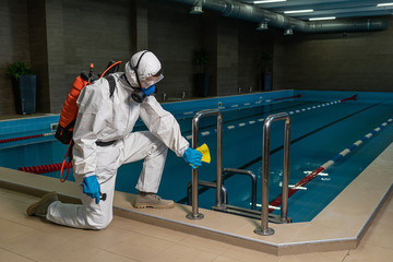 Cleaning and Disinfection in pool amid the coronavirus epidemic Gym cleaning and disinfection Infection prevention and control of epidemic. Protective suit and mask and spray bag COVID-19