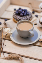 Yammy! Cup of coffee on wooden serving tray and donut with blueberry, morning concept. Selective focus