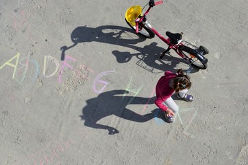 View from the balcony. Little girl writes letters of the English alphabet in colored chalk