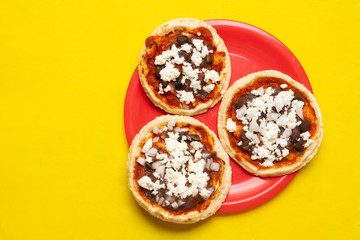 Mexican red sopes with cheese and beans on yellow background