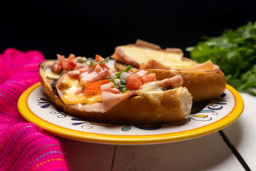 Mexican molletes with ham and cheese on dark background