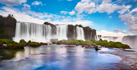 Iguazu waterfalls in Argentina, view from Devil's Mouth. Panoramic view of many majestic powerful water cascades with mist and reflection of blue sky with clouds. Panoramic image of Iguazu valley.