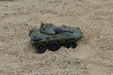 A close up of a Green toy military vehicle on a sand