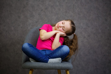 little girl in a pink t-shirt is sitting on a gray chair. Emotional photo of a child
