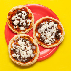Mexican red sopes with cheese and beans on yellow background