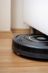 close-up of an old robotic vacuum cleaner on laminate wood floor entering under sofa smart cleaning technology.