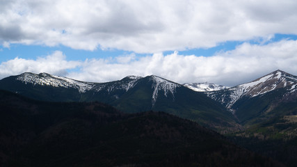Fototapeta premium Snow-capped mountain peaks in the shadow of gray clouds in the sky. Contrast background. Travel and relax