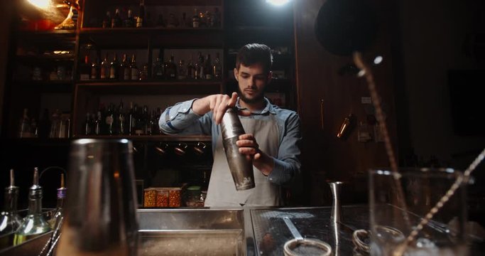 Authentic professional caucasian bartender creating a cocktail drink. Experienced barman pouring alcohol beverage in shaker, then shaking it - food and drink concept close up 4k footage