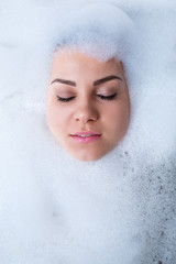 Closeup portrait of a girl in a bathtub and white foam around her face. Different emotions, grimaces, woman smile