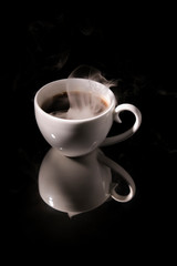 White cup with hot coffee on a black background with reflection.