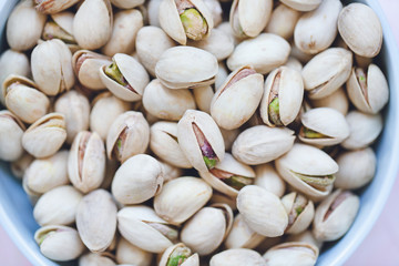 Roasted salted pistachios in shell in bowl on pink background, concept of healthy eating vegan food. Close up, selective focus