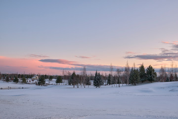 Landscape. The hills are covered with snow with growing trees, a small closed gazebo and a sky with clouds painted with the colors of the sunset.