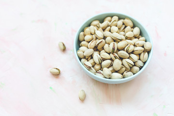 Roasted salted pistachios in shell in bowl on pink background, concept of healthy eating vegan food. Close up, selective focus, copy space