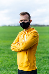 Fototapeta premium Young man in black protective antiviral mask on the street. The guy is resting in the park on a sunny summer day in a mask made by his own hands. Virus protection. Quarantine measures