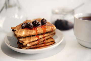 waffles with jam on a white saucer, a Cup of tea on the table and a glass vase with a pine branch